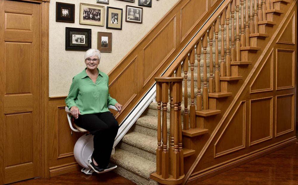 Woman sitting on straight stairlift at bottom of staircase
