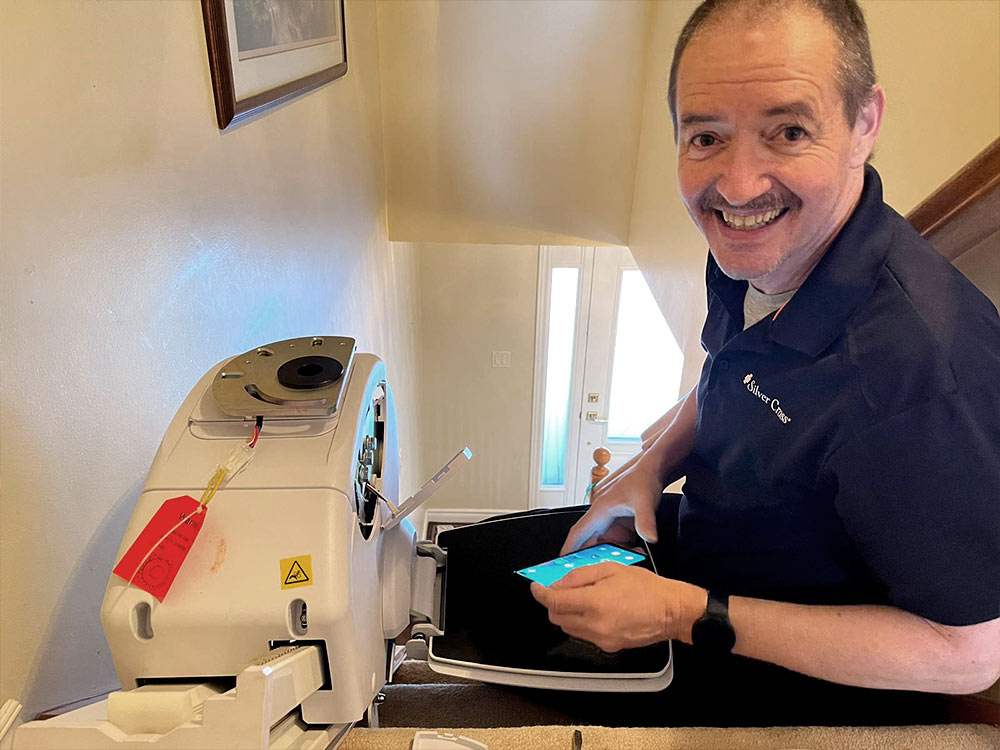Silver Cross stair lift installer smiling while installing unit